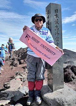 富士山頂上で母校の旗を掲げる卯田先生